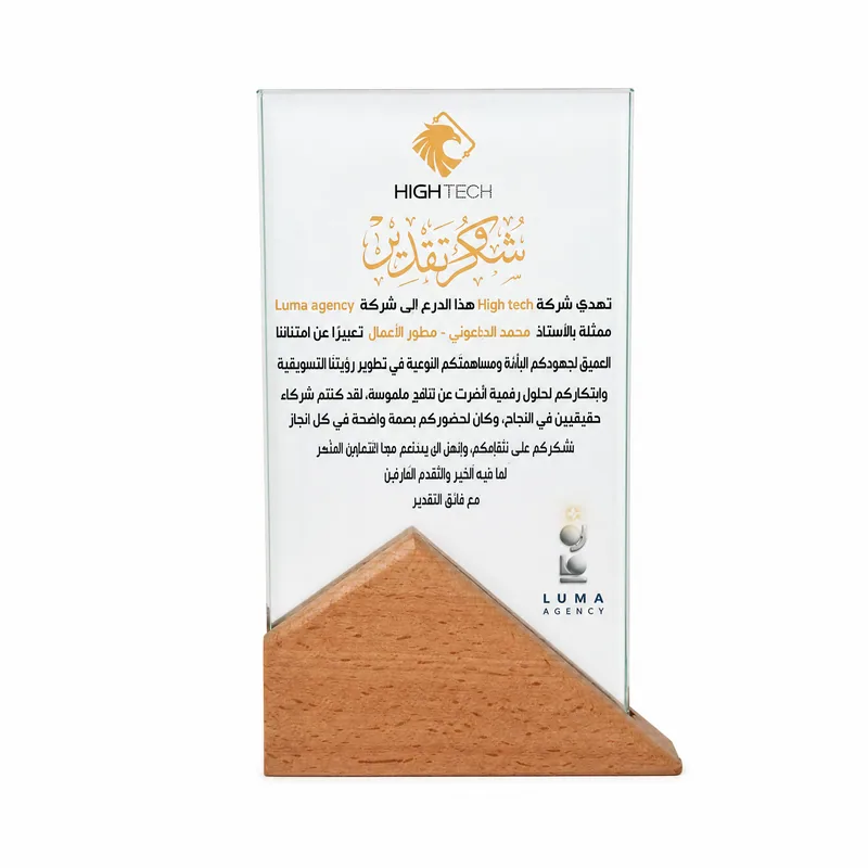 Glass shield on a wooden base presented by High Tech to LUMA Agency, engraved with an Arabic certificate of thanks and appreciation.